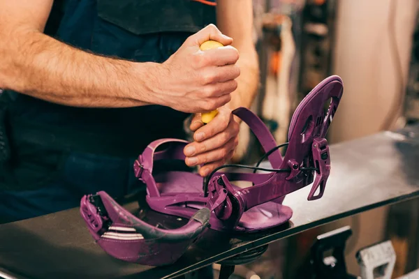 Cropped view of worker screwing snowboard binding to snowboard in repair shop — Stock Photo