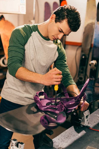 Worker screwing snowboard binding to snowboard in repair shop — Stock Photo