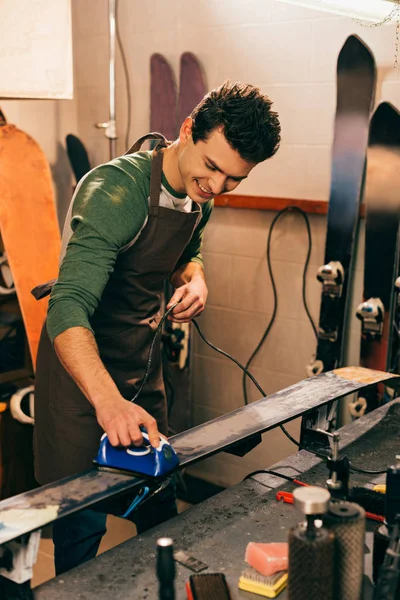 Trabalhador sorrindo esqui encerando com ferro de cera na oficina de reparação — Fotografia de Stock