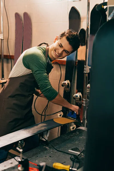 Smiling worker waxing ski with wax iron in repair shop — Stock Photo