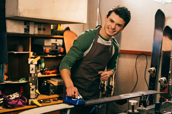 Smiling worker waxing ski with wax iron in repair shop — Stock Photo