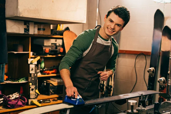 Trabalhador sorrindo esqui encerando com ferro de cera na oficina de reparação — Fotografia de Stock