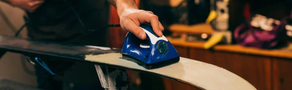 Panoramic shot of worker waxing ski with wax iron in repair shop — Stock Photo