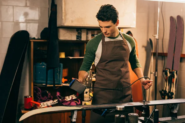 Handsome worker waxing ski with wax iron in repair shop — Stock Photo