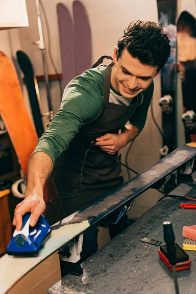 Smiling worker waxing ski with wax iron in repair shop — Stock Photo