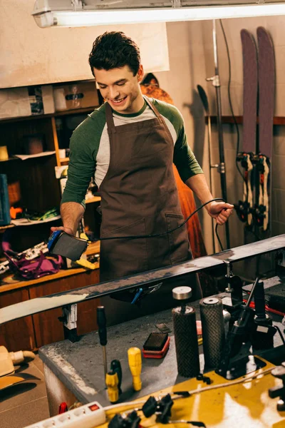 Smiling worker waxing ski with wax iron in repair shop — Stock Photo