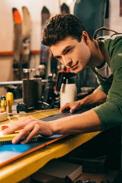 Messa a fuoco selettiva del lavoratore utilizzando pennello su snowboard in officina di riparazione — Stock Photo
