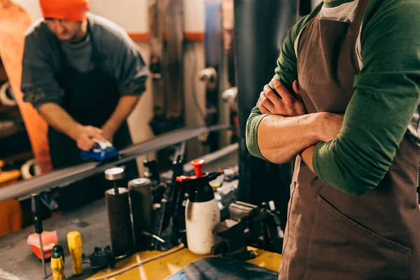 Cropped view of worker with crossed arms and his colleague using wax iron in repair shop — Stock Photo