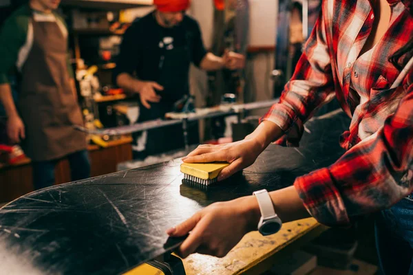 Vista recortada de trabajador pulir snowboard con cepillo en taller de reparación - foto de stock