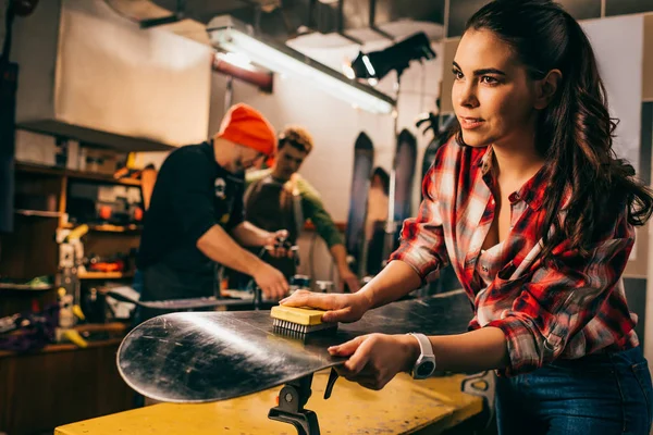 Selective focus of worker polishing snowboard with brush in repair shop — Stock Photo