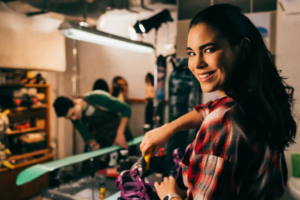 Foco seletivo do trabalhador sorrindo aparafusar snowboard encadernação para snowboard na oficina de reparação — Fotografia de Stock