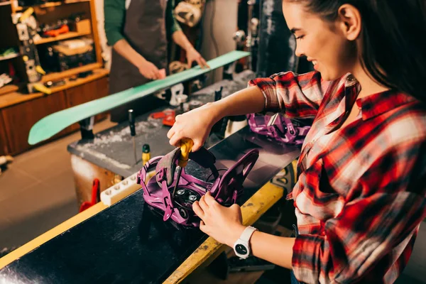 Messa a fuoco selettiva del lavoratore sorridente avvitando legame snowboard allo snowboard in officina di riparazione — Foto stock