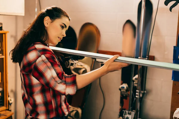 Привлекательная женщина держит и смотрит на лыжи в ремонтной мастерской — стоковое фото
