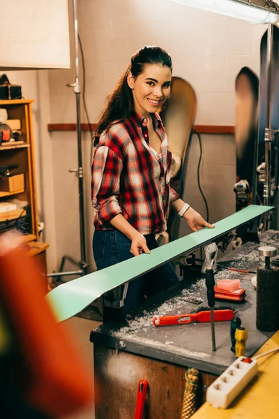 Trabajador sonriente sosteniendo el esquí y mirando a la cámara en el taller de reparación - foto de stock