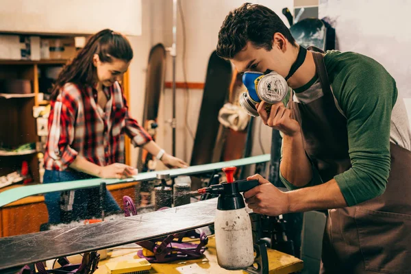 Selective focus of worker in respirator spraying on snowboard in repair shop — Stock Photo