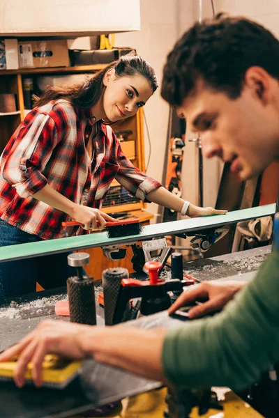 Selective focus of smiling worker cleaning ski and looking at colleague in repair shop — Stock Photo