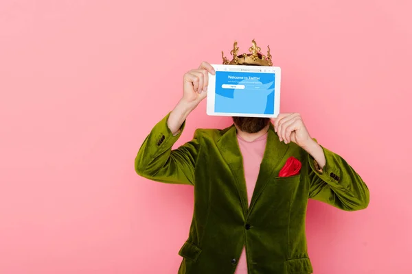Київ, Україна - 3 грудня 2019: чоловік з короною тримає цифровий планшет з посиленим додатком, ізольованим на рожевому — стокове фото