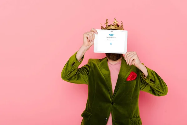 KYIV, UCRAINA - 3 DICEMBRE 2019: uomo con corona che tiene tablet digitale con app skype isolata su rosa — Foto stock
