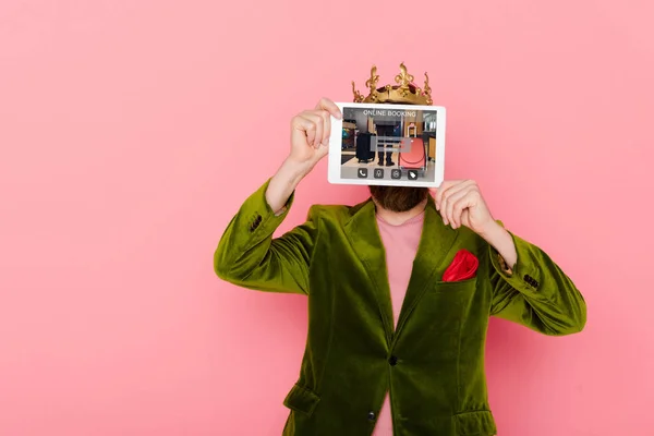 Man with crown holding digital tablet with online booking isolated on pink — Stock Photo