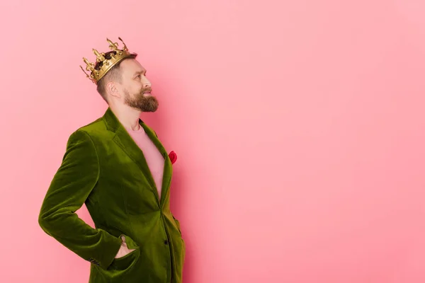 Vista laterale di uomo sorridente con corona in giacca di velluto guardando lontano su sfondo rosa — Foto stock