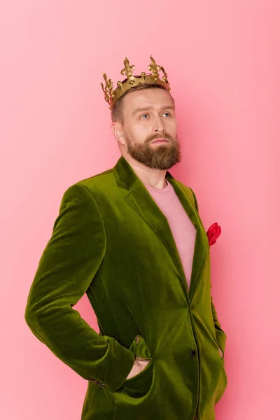 Homem bonito com coroa em casaco de veludo olhando para o fundo rosa — Fotografia de Stock