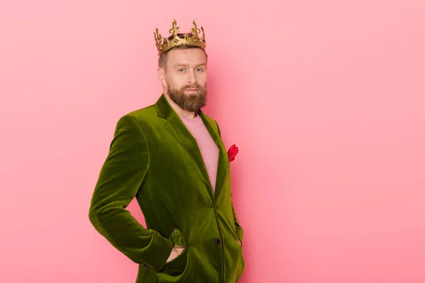 Schöner Mann mit Krone in Velourjacke blickt in die Kamera auf rosa Hintergrund — Stockfoto