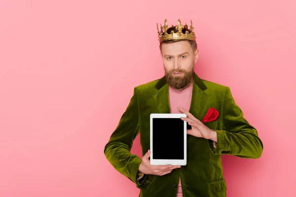 Hombre guapo con corona en chaqueta de terciopelo sosteniendo tableta digital sobre fondo rosa - foto de stock