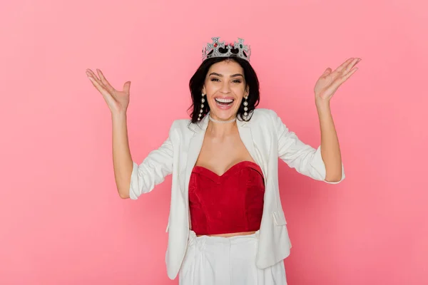 Mujer sonriente con corona mostrando las manos extendidas sobre fondo rosa - foto de stock