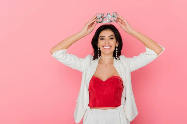 Sonriente mujer sosteniendo corona por encima de la cabeza sobre fondo rosa - foto de stock