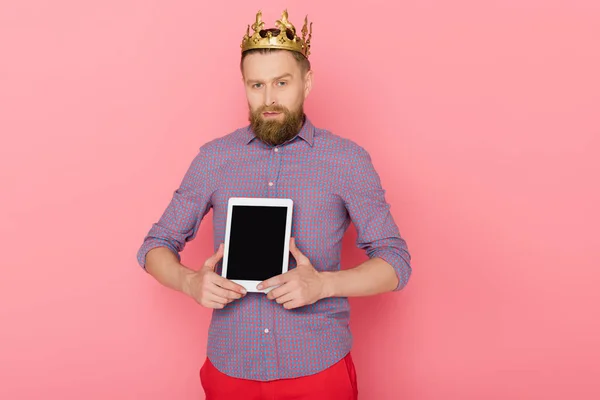 Homem com coroa segurando tablet digital no fundo rosa — Fotografia de Stock