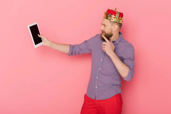 Hombre pensativo con corona mirando tableta digital sobre fondo rosa - foto de stock