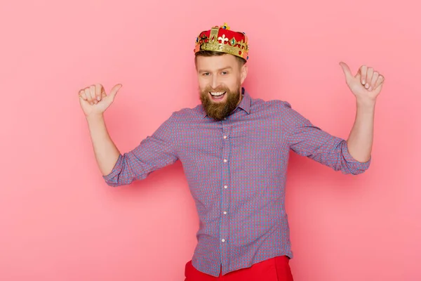 Smiling man with crown showing thumbs up on pink background — Stock Photo