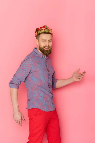 Улыбающийся мужчина с короной, смотрящий на камеру на розовом фоне — стоковое фото