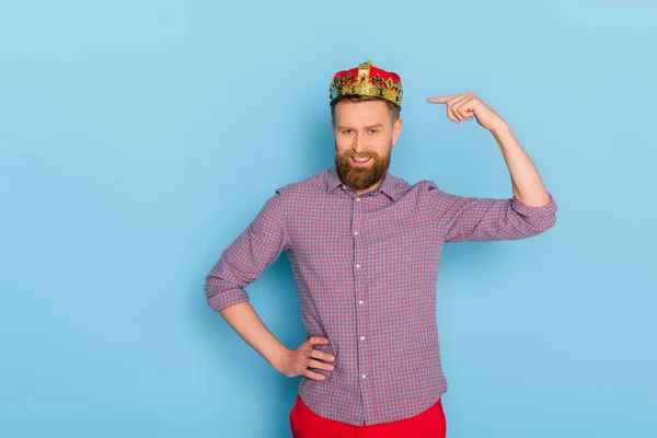 Sonriente hombre apuntando con el dedo a la corona sobre fondo azul - foto de stock