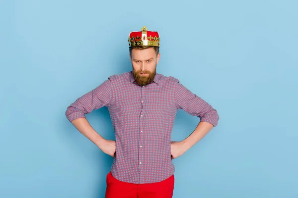 Wütender Mann mit Krone blickt in Kamera auf blauem Hintergrund — Stockfoto