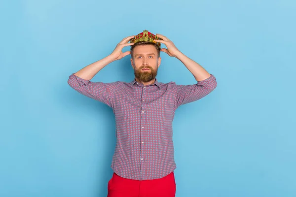 Handsome man in shirt wearing crown on blue background — Stock Photo