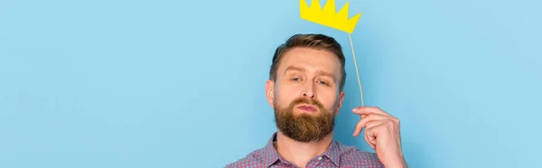 Panoramic shot of man holding paper crown on blue background — Stock Photo