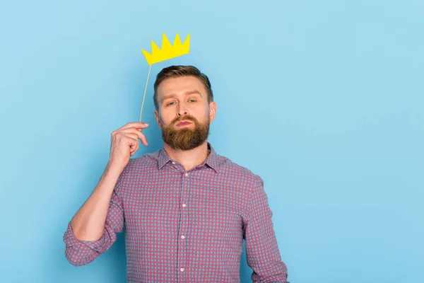 Homem bonito na camisa segurando coroa de papel no fundo azul — Fotografia de Stock