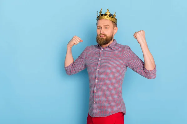 Ernster Mann mit Krone zeigt starke Geste auf blauem Hintergrund — Stockfoto