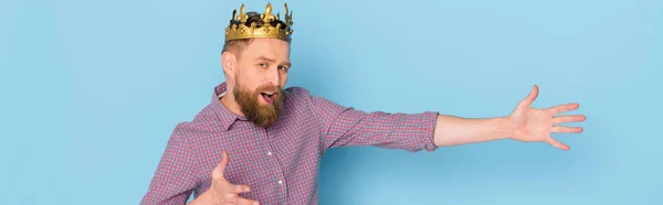 Plano panorámico del hombre conmocionado con la corona apuntando con la mano sobre fondo azul - foto de stock