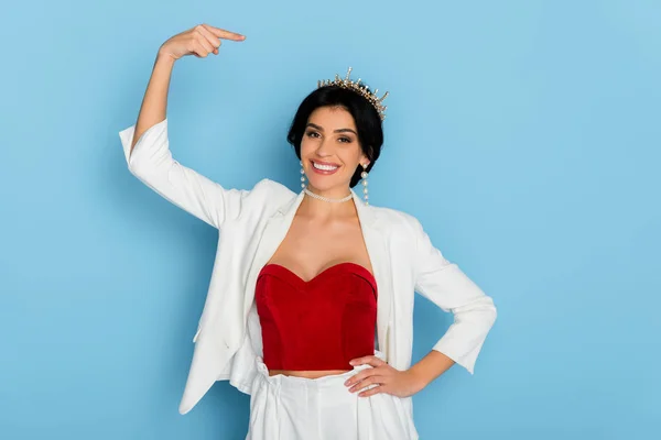 Mujer sonriente señalando con el dedo a la corona sobre fondo azul — Stock Photo