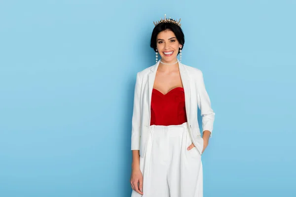 Mujer sonriente con corona mirando a la cámara sobre fondo azul - foto de stock