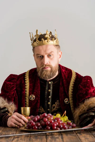 König mit Krone sitzt am Tisch isoliert auf grau — Stockfoto