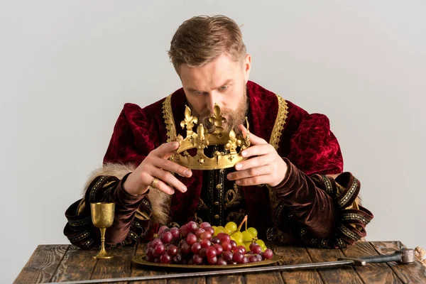 King sitting at table and holding crown isolated on grey — Stock Photo