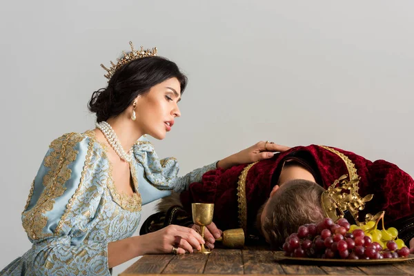 Rainha triste com coroa olhando para rei morto isolado em cinza — Fotografia de Stock