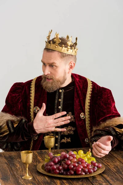 Шокований чоловік з короною сидить за столом ізольовано на сірому — стокове фото