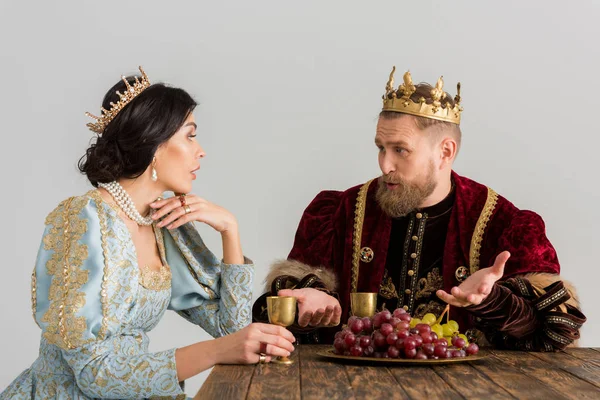 Королева и король с коронами, сидящими за столом и разговаривающими изолированными на сером — стоковое фото