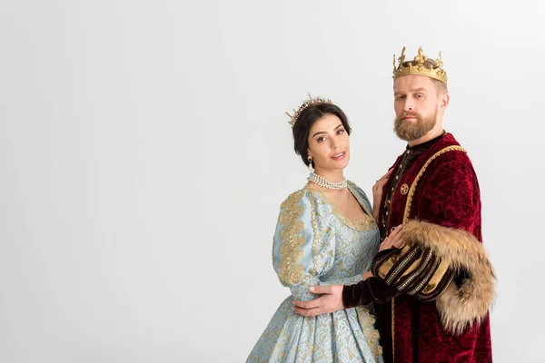 Smiling queen and king with crowns hugging isolated on grey — Stock Photo