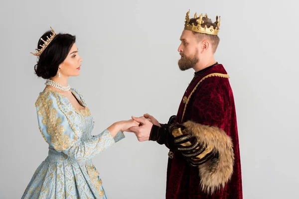 Вид сбоку королевы и короля с коронами, держащими руки в изоляции на сером — стоковое фото