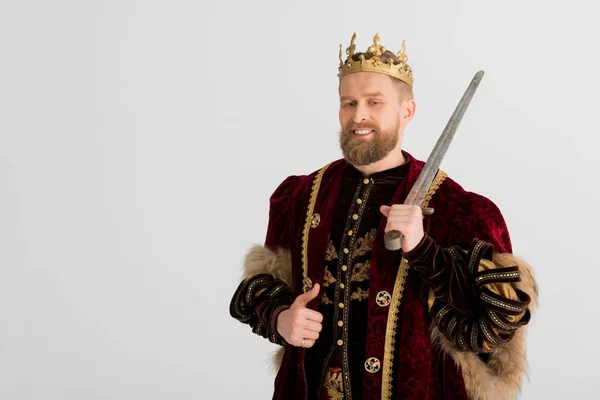 Rey sonriente con corona sosteniendo la espada y mostrando como aislado en gris - foto de stock